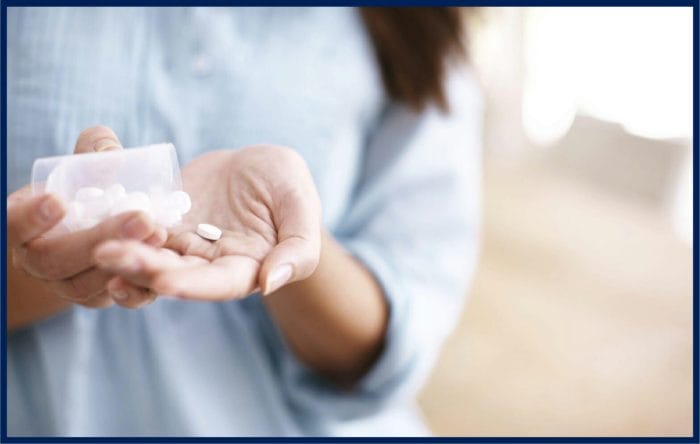 A woman's hand holding a bottle of medicine pills and capsules.